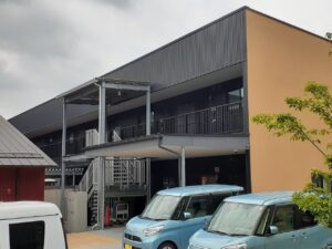 2階建ての介護施設の外観。駐車スペースと玄関が見える